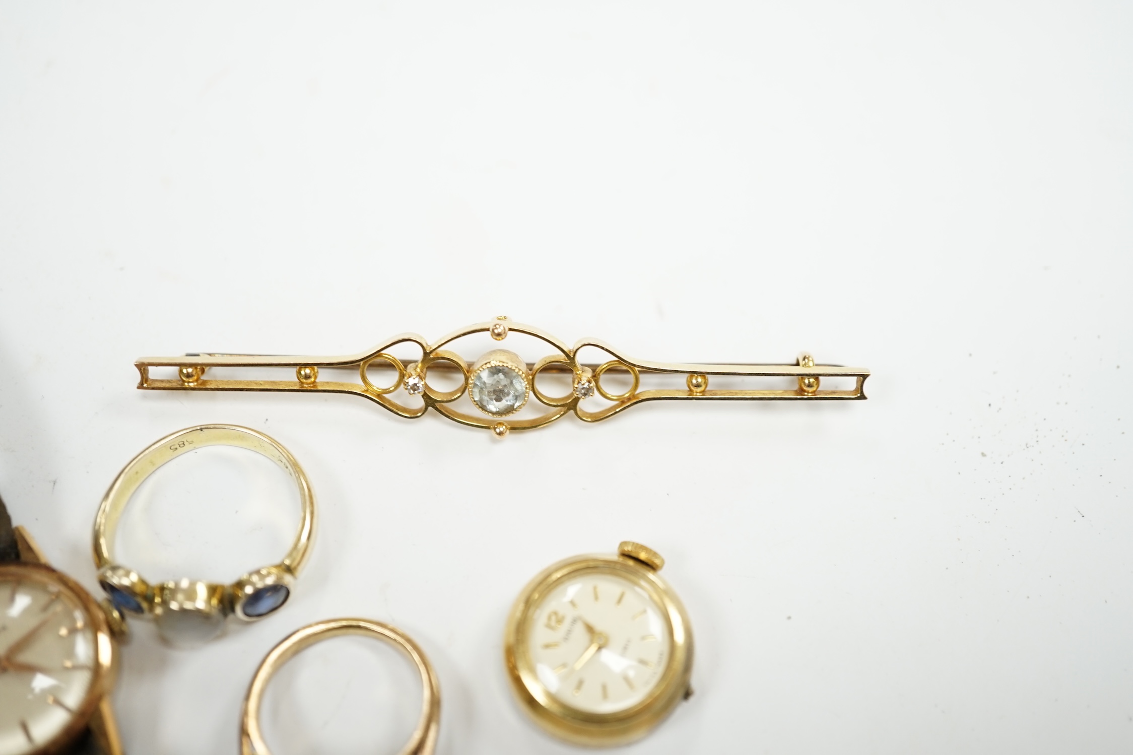 An Edwardian 15ct, aquamarine and diamond set three stone bar brooch, 74mm, a lady's yellow metal Omega manual wind wrist watch, a lady's rolled gold wrist watch a 14k and three stone sapphire ring the central stone a wh